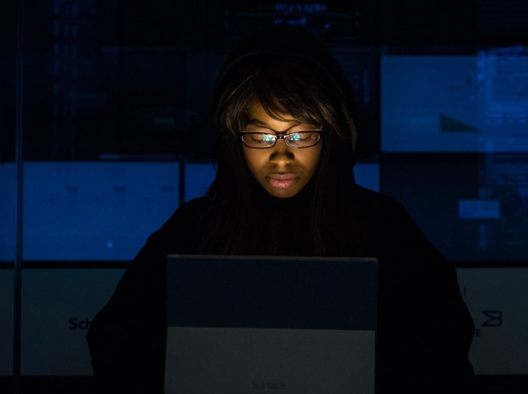 Kvinna med glasögon och mörka kläder med laptop på mörkt kontor Tele2 Företag