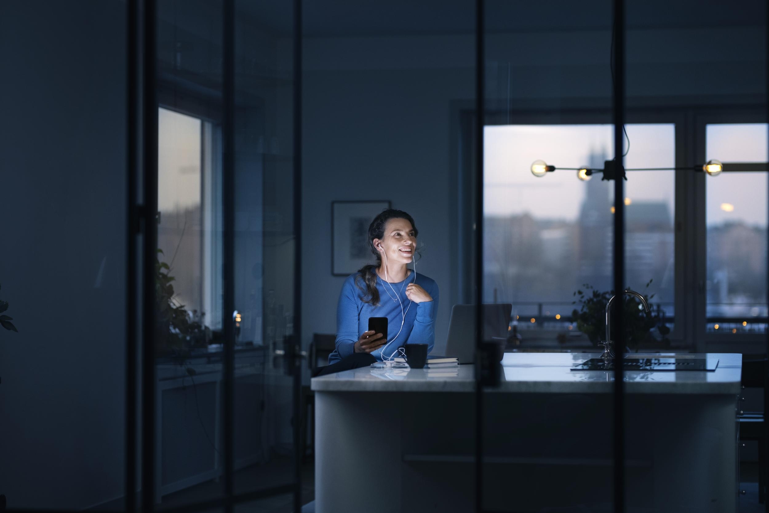 Ung kvinna i blå tröja sitter med mobil vid köksö.